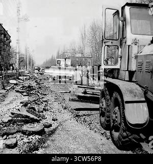 Una brigata di operaie posa manualmente pietre per un nuovo marciapiede in via Shevchenko a Sloviansk, RSS Ucraina, in questa potente foto del 1980. Le donne, vestite con semplici abiti da lavoro e velo, utilizzano martelli per posizionare le piastrelle. Questa autentica immagine in bianco e nero documenta il lavoro fisicamente impegnativo coinvolto nei progetti di rinnovamento urbano e mette in evidenza il ruolo cruciale, spesso invisibile, delle donne nel lavoro di costruzione manuale in Unione Sovietica Foto Stock