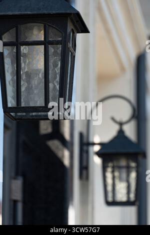 Foto ravvicinata delle classiche lanterne da parete in metallo nero montate su una facciata moderna dell'edificio. L'immagine cattura le trame e le ombre create da Natural Foto Stock
