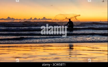 Pescatori balinesi che lanciano la rete nel surf al tramonto a Seminyak Beach, Bali, Indonesia Foto Stock