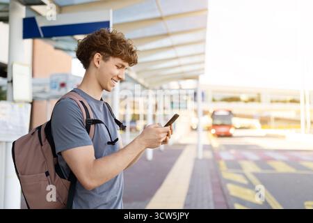 Vista laterale del viaggiatore sorridente che utilizza lo smartphone sulla piattaforma dell'aeroporto Foto Stock