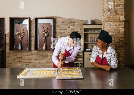 Esperto panettiere che riempie l'impasto di pasta mentre l'apprendista osserva Foto Stock