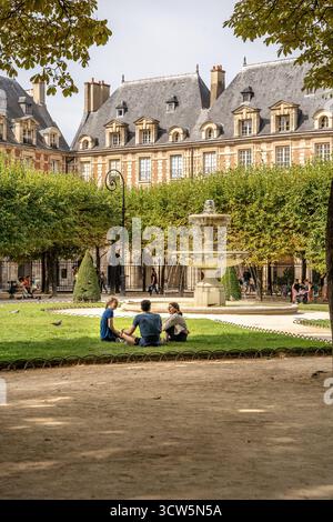 Persone che si rilassano sull'erba a Place des Vosges nel quartiere Marais durante una giornata estiva, una delle piazze più antiche e belle di Parigi, in Francia Foto Stock