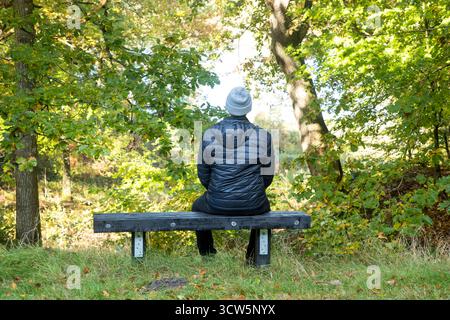 immagine di solitudine di un uomo seduto da solo sulla panchina nella foresta che guarda al paesaggio pensando, immagine di molti significati, calma, destrezza, triste, felice, pace Foto Stock