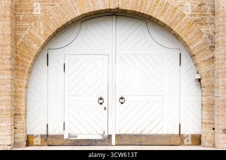Un'immacolata porta doppia ad arco bianca posta all'interno di un arco in mattoni, che offre un'elegante e storica entrata ad un edificio. L'immagine trasmette un arco classico Foto Stock
