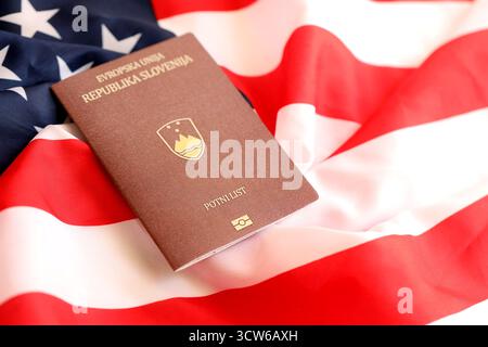 Passaporto sloveno sulla grande bandiera ondulata degli Stati Uniti d'America primo piano. Concetto di immigrazione e visto PER GLI STATI UNITI Foto Stock