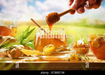 Preparare un infuso naturale a mano, versare il miele in una tazza con zenzero e prodotti biologici e un fondo naturale. Vista frontale. Foto Stock