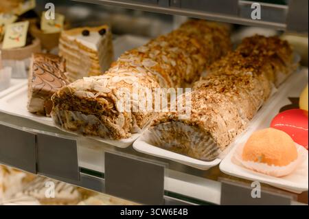Panini da dessert con guarnizioni di mandorle e noci esposti in una vetrina da forno. Una varietà di torte e dessert con glassa e noci su un ripiano di vetro i. Foto Stock