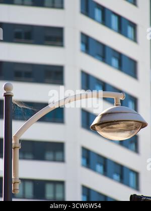 Lampione urbano sulla facciata del moderno edificio - Un lampione bianco con una ragnatela in forte risalto contrasta con l'offuscata, geometrica e moderna high-ri Foto Stock
