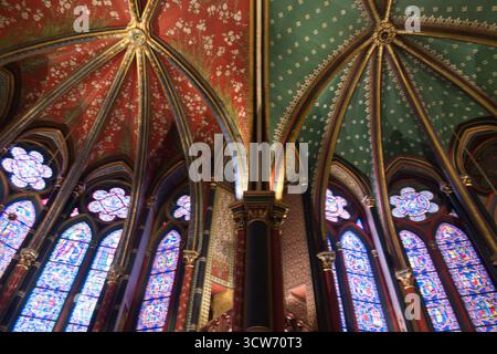 Volte gotiche e murales di Sainte-Chapelle - Vista a basso angolo di volte gotiche riccamente dipinte in rosso, oro e tè, accanto a un grande crocifisi Foto Stock