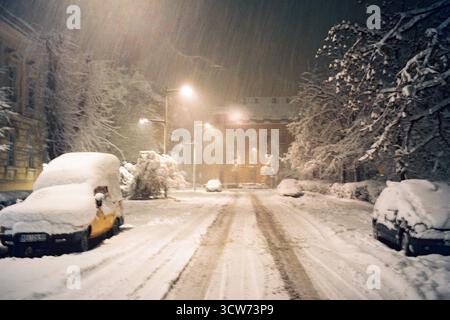 Nevosa notte invernale, piste fresche su una strada non arata. Caduta di neve pesante, illuminata da un unico semaforo. Atmosfera tranquilla, fredda e analogica. Foto Stock
