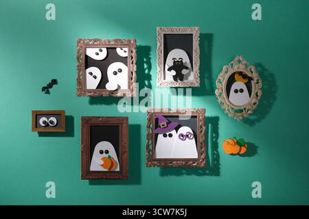 Decorazioni di Halloween fatte a mano. Una parete turchese con ritratti di fantasmi con zucche, gatti e pipistrelli. Arte cartacea Foto Stock