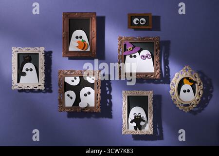 Artigianato di carta fatto a mano per Halloween. Parete viola con ritratti di fantasmi con zucche, gatti e pipistrelli. Arte cartacea. Foto Stock