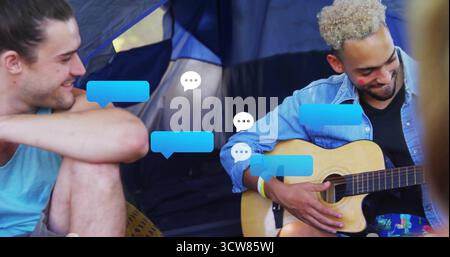 Suona il chitarrista mentre suona la chitarra all'ingresso blu della tenda da da campeggio, con sovrapposizioni di bolle di chat digitali. All'aperto, compagnia, tempo libero, comunicazione, Foto Stock