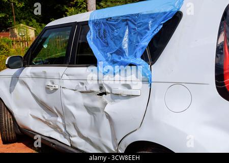 L'auto bianca con danni significativi porta la plastica blu sul finestrino rotto Foto Stock