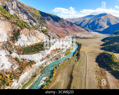 Ampia vista aerea del vibrante e turchese fiume Katun che attraversa una valle, delimitata da scogliere bianche e rosse a contrasto e da pendii autunnali Foto Stock