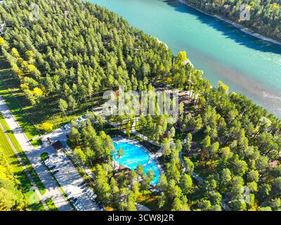 Vista aerea ad alto angolo di un'area del resort caratterizzata da una piscina blu brillante, edifici e un'area parcheggio accanto ad un ampio fiume turchese Foto Stock