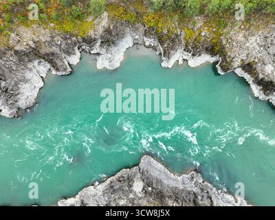 Vista aerea ravvicinata che cattura le potenti, striscianti e vivide acque turchesi del fiume mentre scorre tra le sponde rocciose Foto Stock