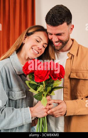 Una coppia gioiosa gode di un momento tenero mentre si abbracciano l'un l'altro, reggendo uno splendido bouquet di rose rosse piene di amore e affetto, creando un Foto Stock