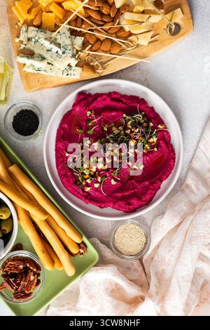 L'hummus di barbabietola è collocato al centro di un tagliere di salumi, circondato da spuntini come olive, noci, formaggio e grissini croccanti. Una luce, invit Foto Stock