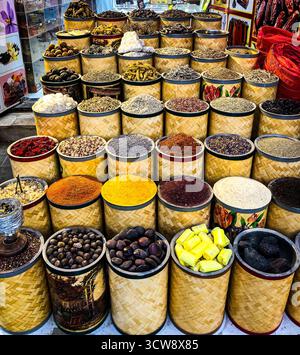 Colorata esposizione di spezie, erbe aromatiche e ingredienti naturali disposti in cesti di bambù intrecciati in un mercato tradizionale. Foto Stock