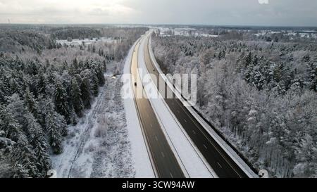 Vista aerea di una tranquilla autostrada coperta di neve che attraversa la foresta invernale Foto Stock