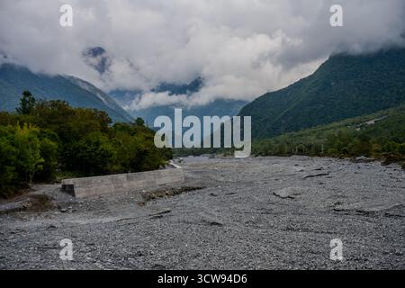 Un ampio letto di fiume secco si snoda attraverso le colline pedemontane dei monti del Caucaso vicino a Shaki, Azerbaigian. Nuvole basse e fitte foreste verdi coprono il surrou Foto Stock