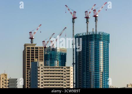 Cantiere con gru che costruiscono un moderno grattacielo di vetro contro un cielo limpido Foto Stock