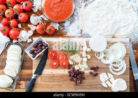 Vista dall'alto dei classici ingredienti della pizza italiana: Mozzarella, farina, aglio, salsa di pomodoro, olive, e cipolle, predisposte per la preparazione della cottura in casa. Foto Stock