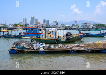 NHA TRANG, VIETNAM - 25 APRILE 2025. Barche da pesca sul fiume Cai, il ponte, grattacieli e bandiere nazionali Foto Stock