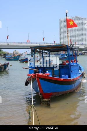NHA TRANG, VIETNAM - 25 APRILE 2025. Barche da pesca sul fiume Cai, il ponte, grattacieli e bandiere nazionali Foto Stock