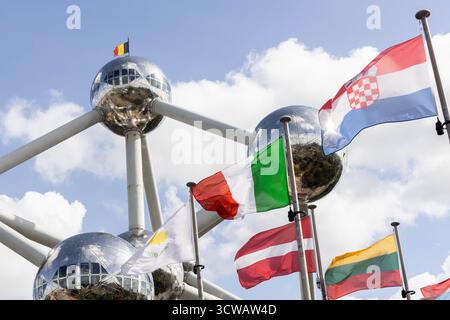 Le bandiere di diversi stati membri dell'Unione europea ondeggiano davanti all'Atomium di Bruxelles, con la bandiera belga sopra. A partire dal 12 ottobre 2025 il nuovo sistema di ingressi/uscite (EES) dell'Unione europea sostituirà il timbro del passaporto con la registrazione biometrica (impronte digitali sul volto) per i viaggiatori extracomunitari, compresi i britannici. Crediti: Sinai Images/Alamy Live News Foto Stock