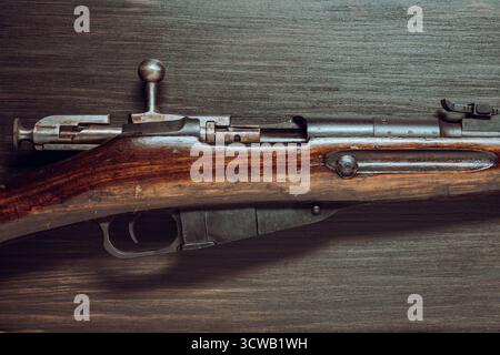 Dettaglio del fucile Mosin sovietico su uno sfondo di legno, primo piano. L'arma dell'esercito rosso e della rivoluzione. Una carabina d'epoca della seconda guerra mondiale Foto Stock