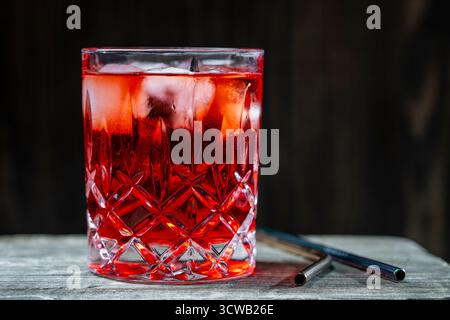 Cocktail rosso in vetro di cristallo su sfondo di legno, primo piano. Bevanda ghiacciata estiva - tè o succo di frutta con cubetti di ghiaccio su un tavolo di legno, spazio copia Foto Stock