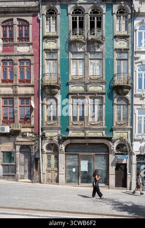 Porto, Portogallo; 14 agosto 2025: Vista sulla strada degli edifici storici di Porto, con facciata piastrellata verde e rossa e balconi in ferro battuto , la gente cammina Foto Stock