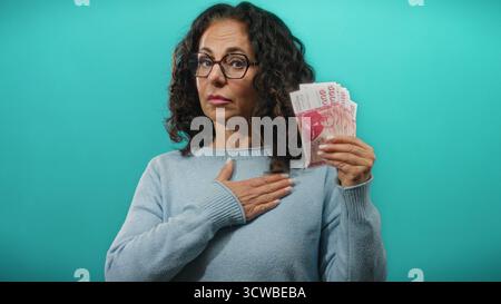 Donna di mezza età che tiene in mano banconote della corona islandese mentre alza la mano con un gesto di giuramento su uno sfondo blu. Foto Stock