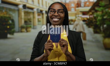 Una donna in maglia gialla ha il passaporto australiano sorridente sulla strada urbana, rappresentando la felicità dei viaggi e la diversità culturale in una città all'aperto setti Foto Stock