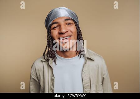 il ritratto di un giovane uomo allegro sorride ampiamente, mostrando le sue bretelle mentre indossa un copricapo argentato su sfondo beige Foto Stock