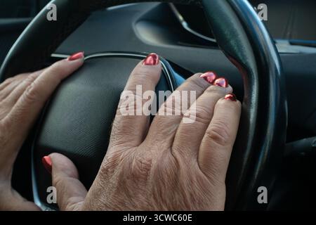 le mani di un vecchio con rughe dell'età e una manicure femminile rossa. Unghie allungate sulle mani degli uomini. Le mani degli uomini con le unghie rosse giacciono sul volante di un Foto Stock