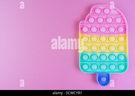 Colorato giocattolo arcobaleno a forma di gelato su sfondo rosa, giocattolo sensoriale riservato per sollievo dallo stress e divertimento Foto Stock