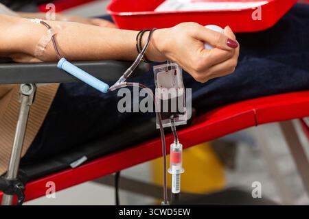 Chiudere la mano di una donatrice di sangue che sprema la palla di gomma durante il processo di trasfusione di sangue Foto Stock