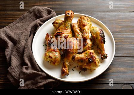 Cosce di pollo arrosto su piatto bianco su fondo marrone in legno. Vista ravvicinata Foto Stock