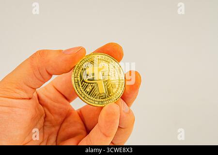 L'immagine raffigura una moneta fisica Tether, progettata in modo complesso come metallo prezioso, tenuta da una mano umana su uno sfondo semplice utilizzato per criptovaluta Foto Stock