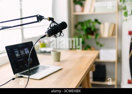 Moderna configurazione di registrazione podcast con microfono e laptop sulla scrivania in studio domestico Foto Stock