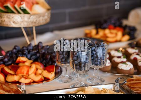 Uno shot vivace e ravvicinato di un piatto di frutta splendidamente organizzato con mirtilli serviti in bicchieri delicati insieme a frutta assortita, biscotti, Foto Stock