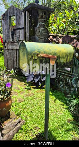 Foto di una vecchia cassetta postale in metallo verde montata su un palo in un giardino. La cassetta postale mostra le texture e le macchie di muschio, conferendole un aspetto rustico e ag Foto Stock