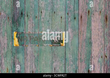 Una recinzione in legno verde e resistente agli agenti atmosferici mostra i resti sbiaditi di un cartello "nessun parcheggio". Il contorno del cartello è visibile, con tracce di vernice gialla Foto Stock