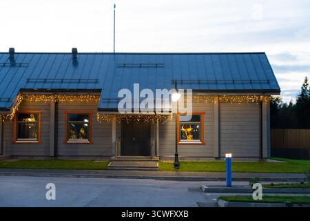 Altai, Russia - 13 maggio 2024: Facciata anteriore di un semplice edificio in legno con tetto in metallo e finestre rivestite di arancione, decorate con luci a corda e. Foto Stock
