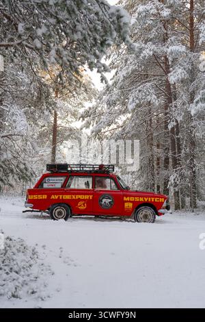 Oblast di Murmansk, Russia - 13 dicembre 2024: Vista laterale di una station wagon rossa Moskvich con un portapacchi, parcheggiata su una pista innevata circondata Foto Stock