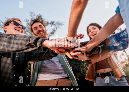Punto di vista a basso angolo di un gruppo di amici diversi che si stringono le mani insieme in un huddle per mostrare il lavoro di squadra, l'unità e il sostegno. Foto Stock