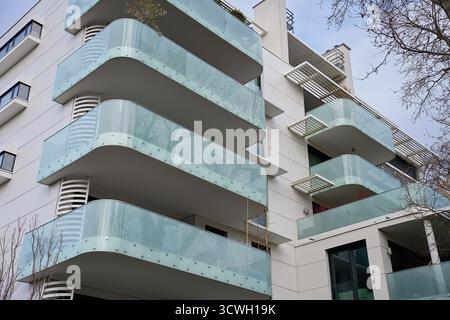 Vista ad angolo basso del moderno edificio residenziale con balconi curvi in vetro e facciata bianca. Edificio di appartamenti contemporaneo nella città europea. Concetto Foto Stock
